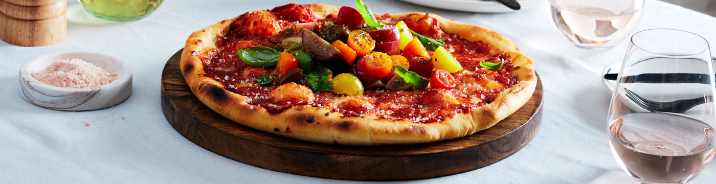 heirloom tomato & basil margherita pizza served on a wooden board at a restaurant table.