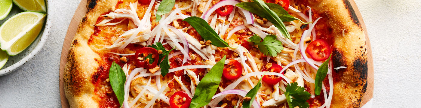 Thai Chicken Pizza on a white pizza paddle, with a bowl of fresh chilli beside it ready to eat.